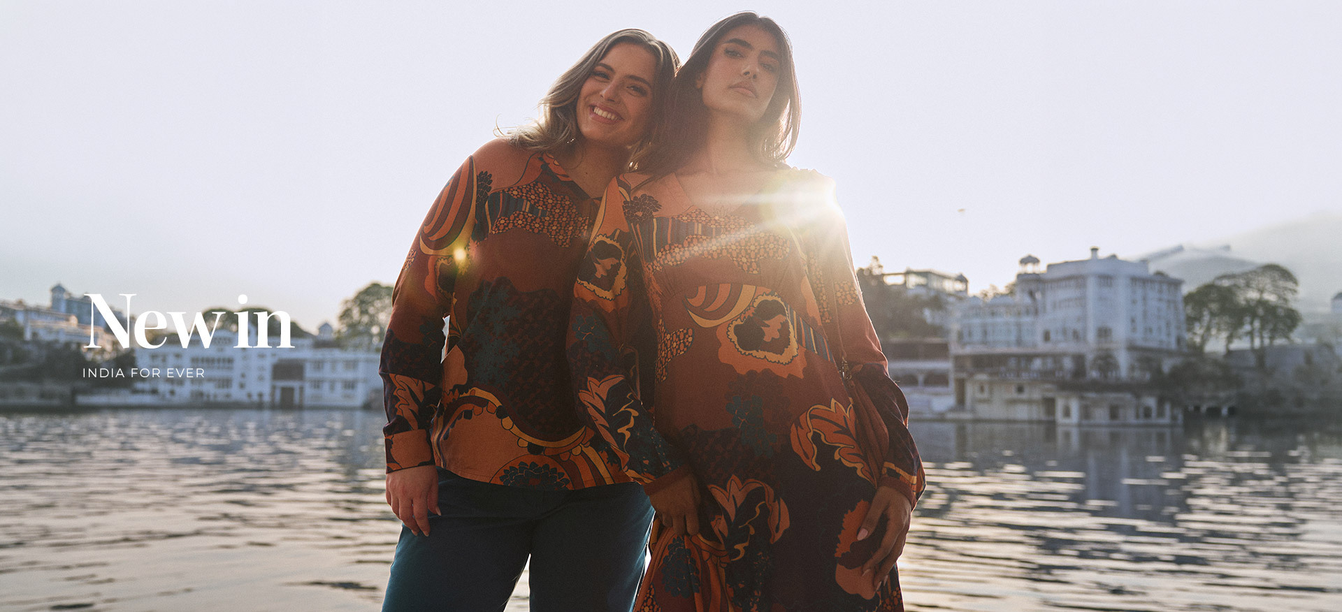 two-women-posing-by-the-water-at-sunset-wearing-patterned-clothing-from-the--new-in---india-for-ever--collection-in-shades-of-brown-orange-and-ochre-